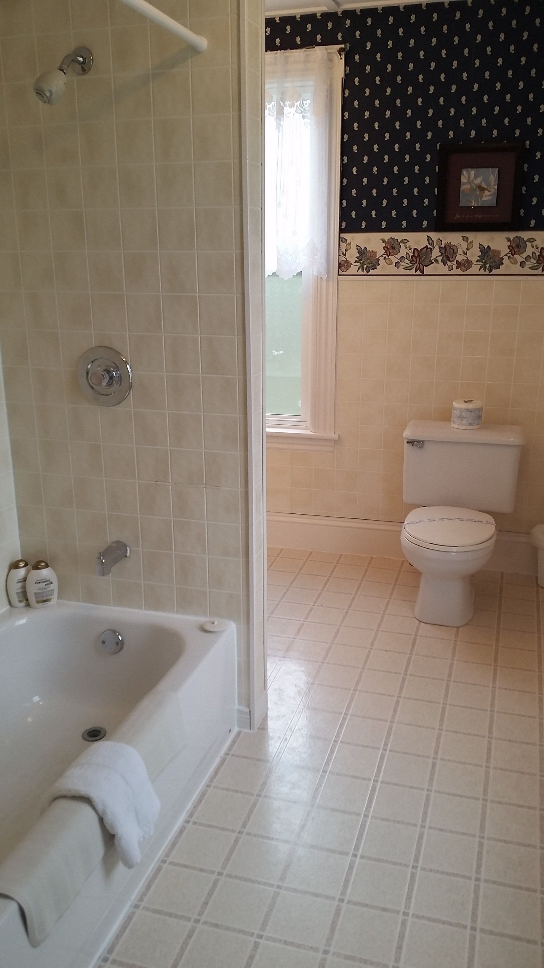 A bathroom with a bathtub, toilet, and a window with a floral curtain.