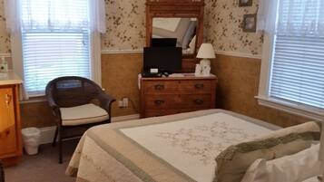 A bedroom with a bed, a dresser, a chair, a mirror, and a window with blinds.