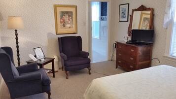 Una habitación de hotel con cama, una silla, cómoda, lámpara y televisor.
