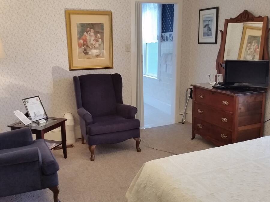 Una habitación de hotel con cama, una silla, cómoda, lámpara y televisor.