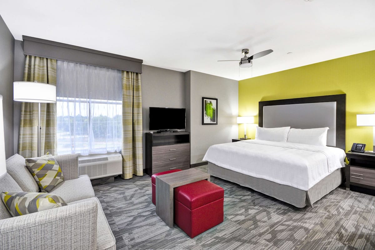 A hotel room with a bed, a TV, a desk, a chair, and a window with curtains.