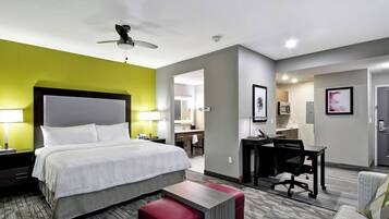 A hotel room with a large bed, a desk, a chair, and a red bench.