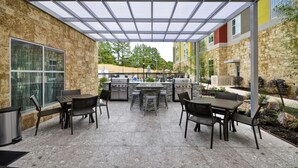 An outdoor patio with stone walls, a grill, and seating. - Homewood Suites by Hilton Tyler (Tyler)