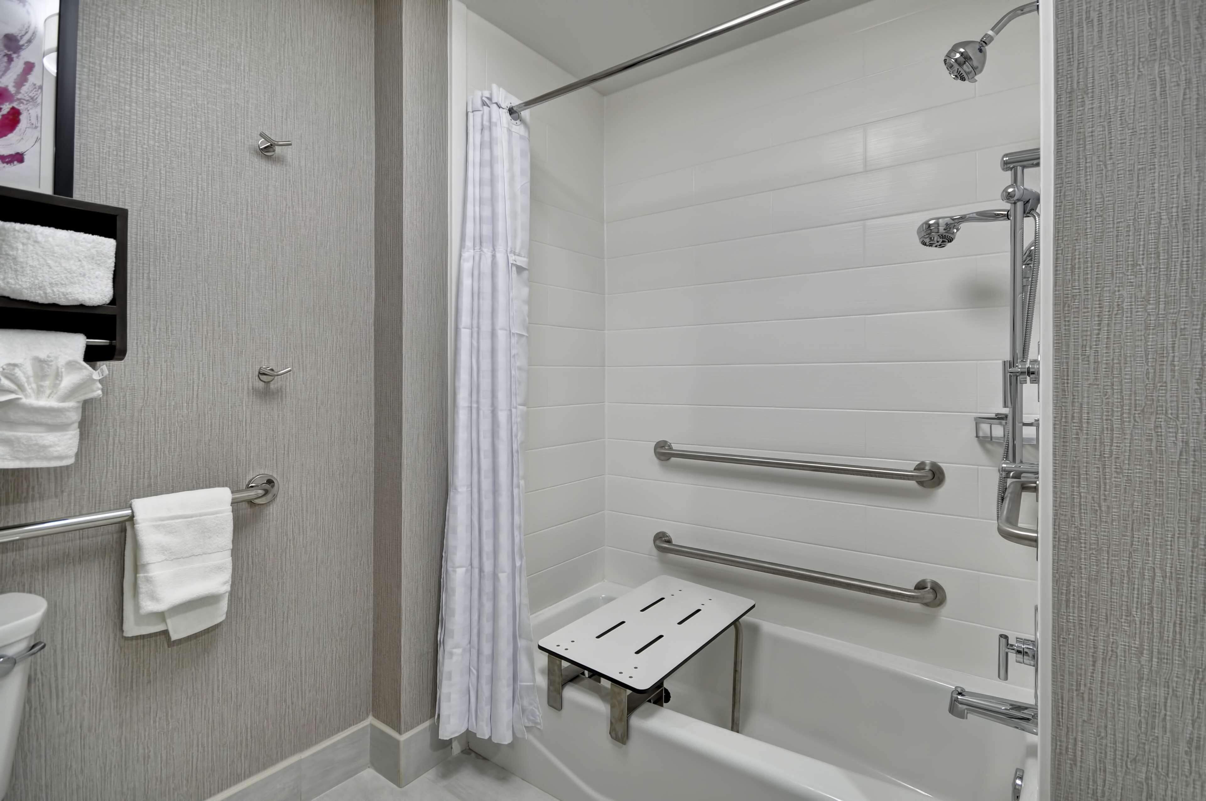 A modern bathroom with a walk-in shower, grab bars, a white towel rack, and a small step for accessibility.