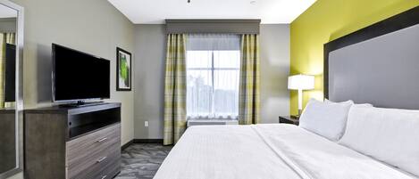 A hotel room with a bed, a TV on a dresser, a ceiling fan, and a window with curtains.