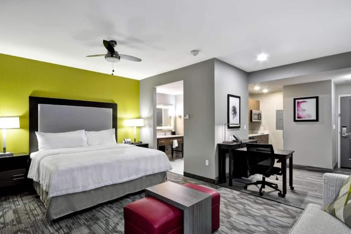 A hotel room with a bed, desk, chair, and a red bench.