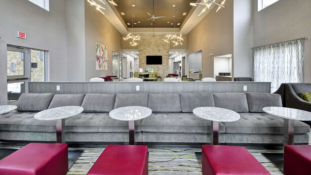 A spacious lobby with a grey sofa, red chairs, and round tables. - Homewood Suites by Hilton Tyler (Tyler)
