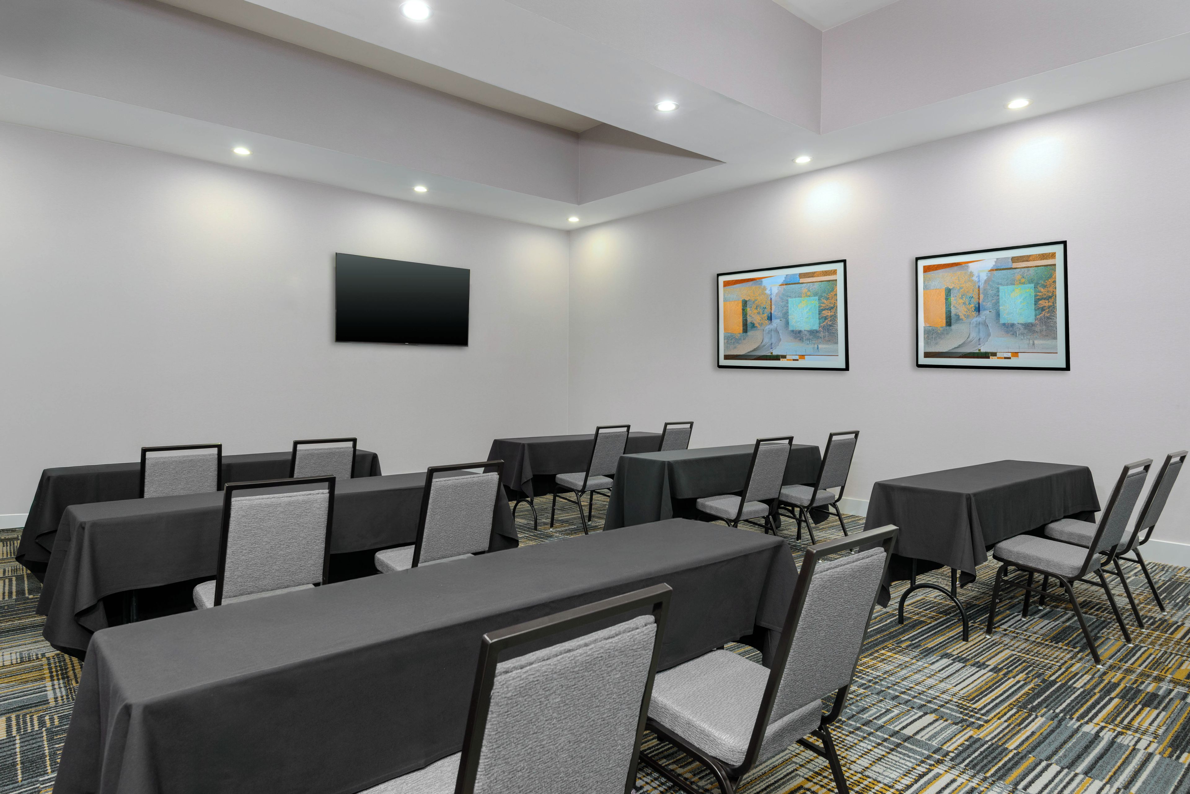 Un salón de conferencias con mesas y sillas, un televisor de pantalla plana y dos cuadros en la pared.