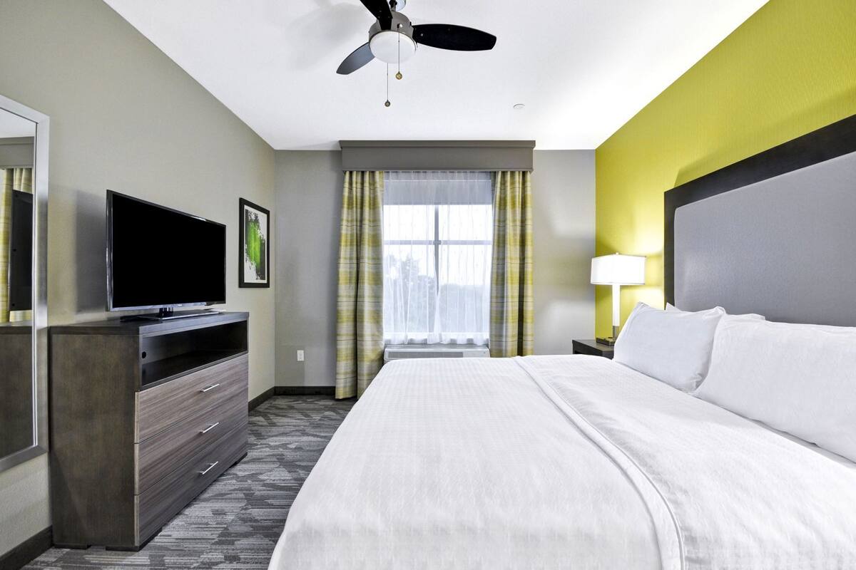 Een hotelkamer met een bed, televisie, bureau, lamp en raam met gordijnen.