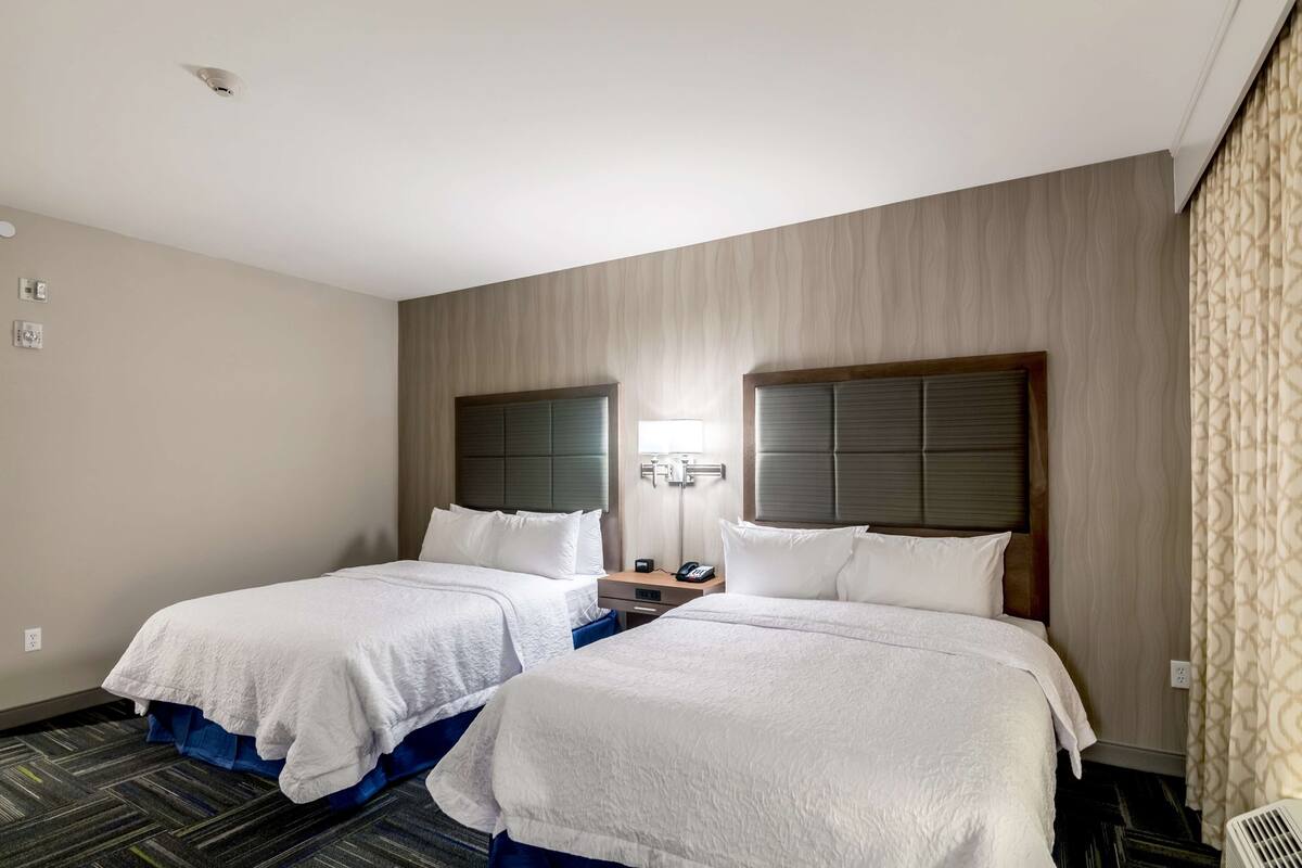 A hotel room with two beds, a nightstand, a lamp, and a patterned curtain.