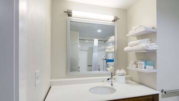 A modern bathroom with a white sink, a large mirror, and shelves with towels and toiletries.