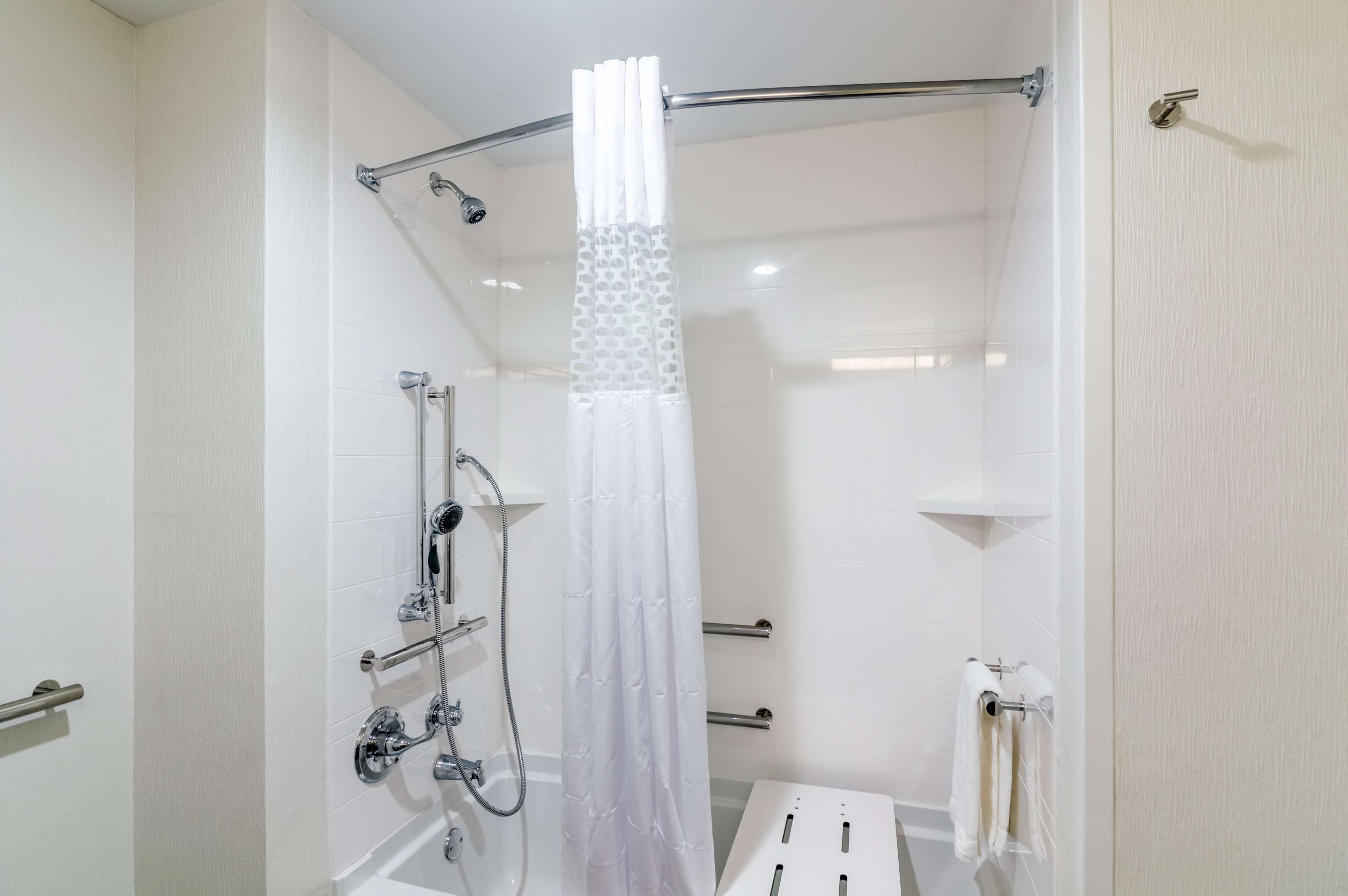 A modern bathroom with a walk-in shower, grab bars, a towel rack, and a toilet with a paper towel dispenser.