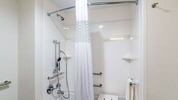 A modern bathroom with a walk-in shower, grab bars, a towel rack, and a toilet with a paper towel dispenser.
