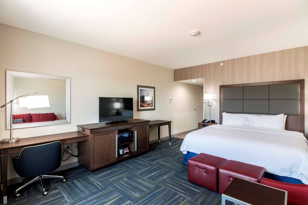 A hotel room with a bed, desk, chair, television, and a large mirror.