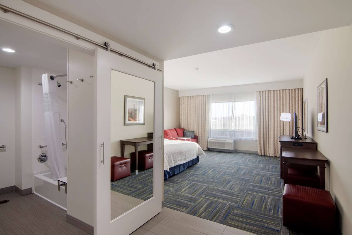 A hotel room with a shower, a bed, a desk, and a window with curtains.