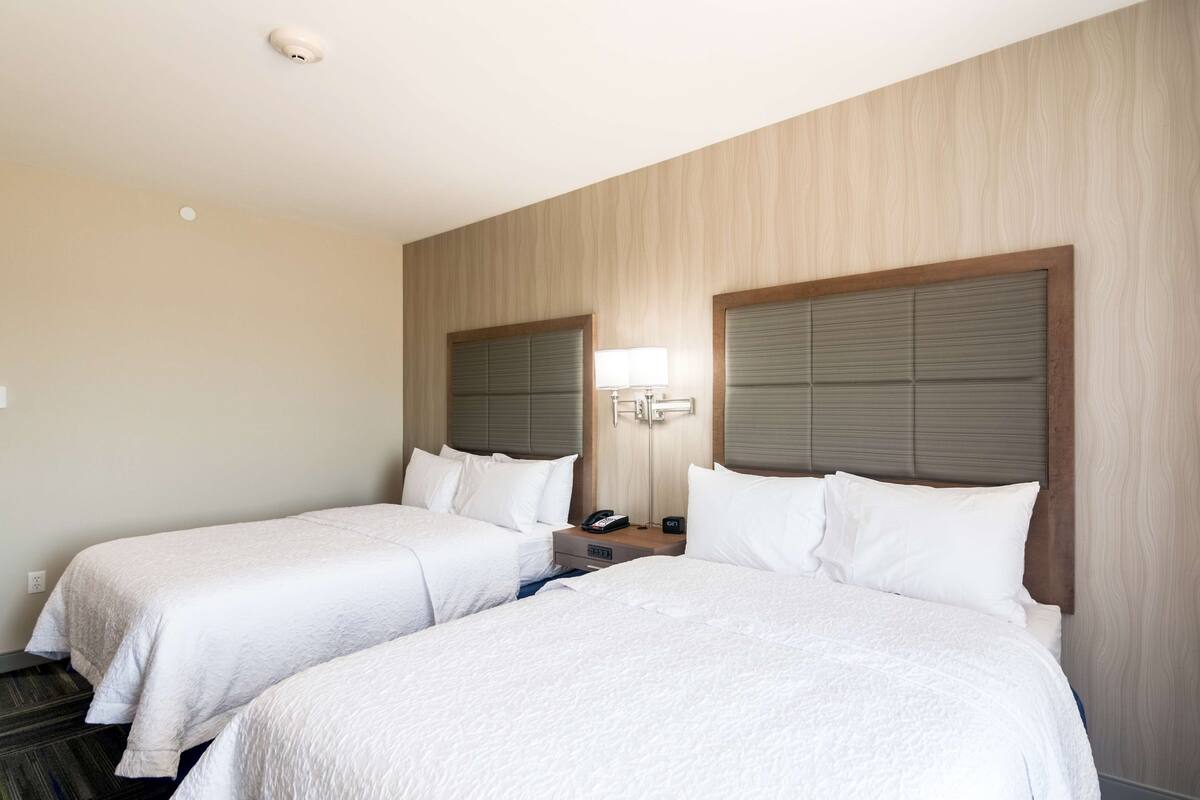 A hotel room with two beds, a nightstand, a lamp, and a telephone.