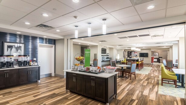A modern kitchen with a central island, a dining area with yellow chairs, and a bar area with a TV.