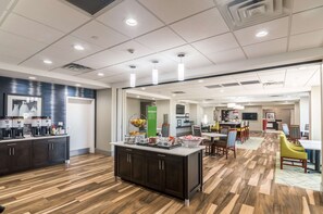 A modern kitchen with a central island, a dining area with yellow chairs, and a bar area with a TV. - Hampton Inn Oklahoma City Northeast (Oklahoma City)
