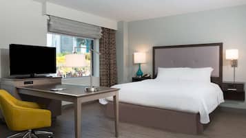 Una habitación de hotel con una cama, un escritorio con televisor, una silla y dos lámparas de noche.