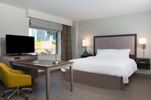 A hotel room with a bed, a desk with a TV, a chair, and two bedside lamps.