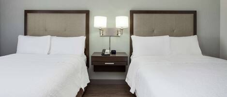Una habitación de hotel con dos camas, una mesita de noche con lámpara y teléfono.