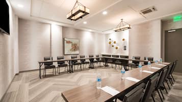Uma sala de conferências com uma mesa comprida, cadeiras e garrafas de água.