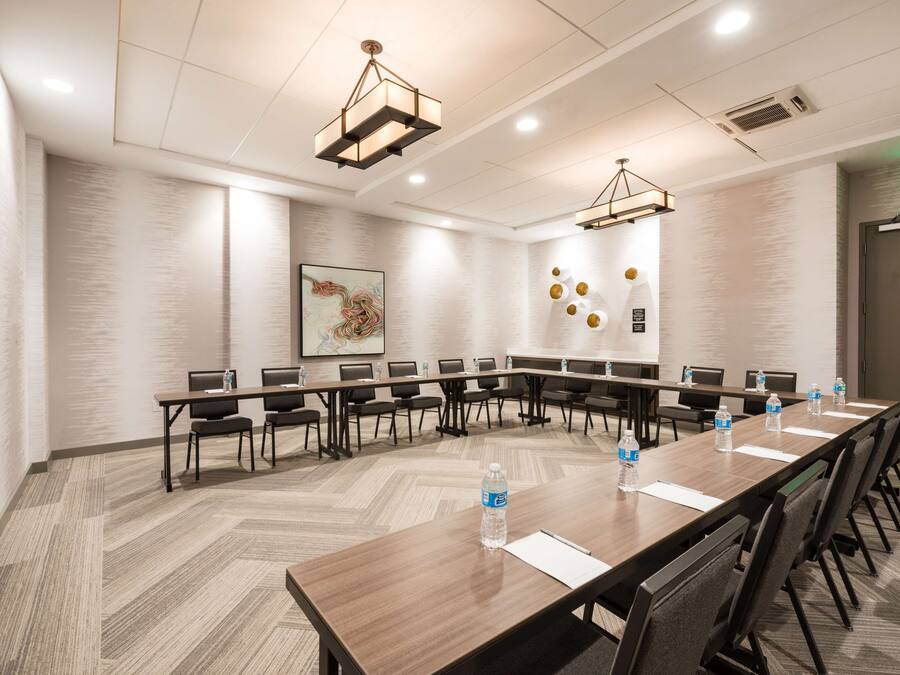Uma sala de conferências com uma mesa comprida, cadeiras e garrafas de água.