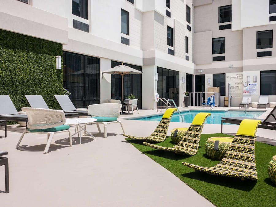 Área de piscina no terraço com espreguiçadeiras, mesa de bilhar e parede verde.