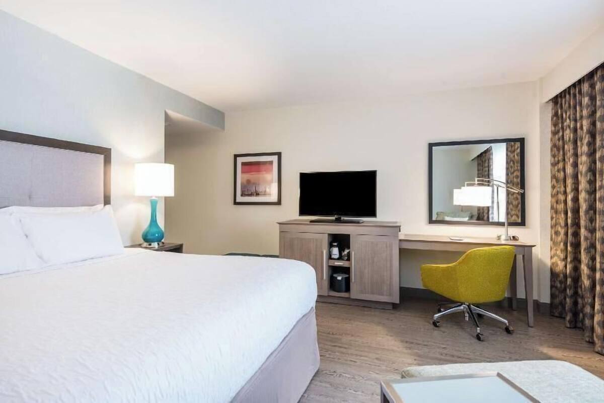 A hotel room with a bed, desk, chair, TV, and a mirror.