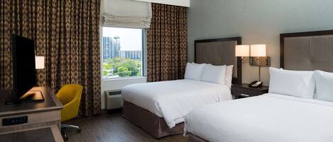 A hotel room with two beds, a desk with a TV, a chair, and a window with curtains.