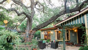 A patio area with outdoor furniture, a large tree, and a building with a porch. - Park Lane Guest House (Austin)