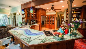 A kitchen with wooden cabinets, a central island with a mosaic tile top, a refrigerator, and a ceiling fan. - Park Lane Guest House (Austin)