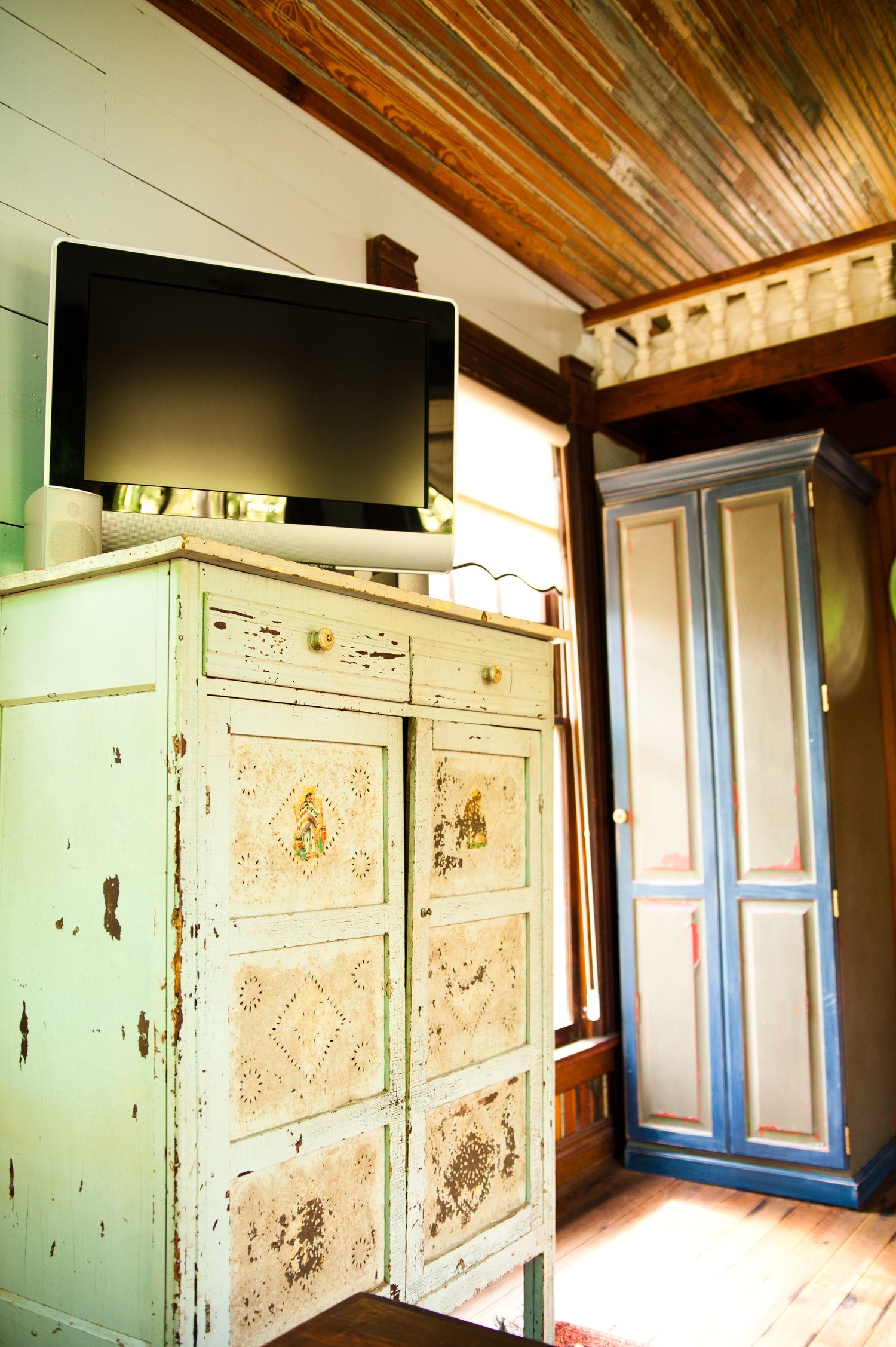 Una habitación con un aparador verde antiguo, un televisor encima y un armario azul.