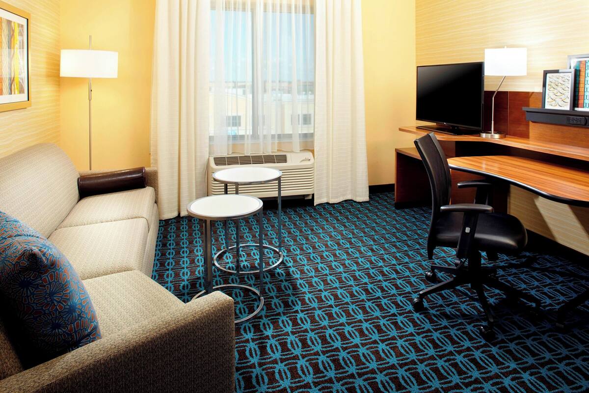 A hotel room with a sofa, a small round table, a TV, and a desk with a chair.