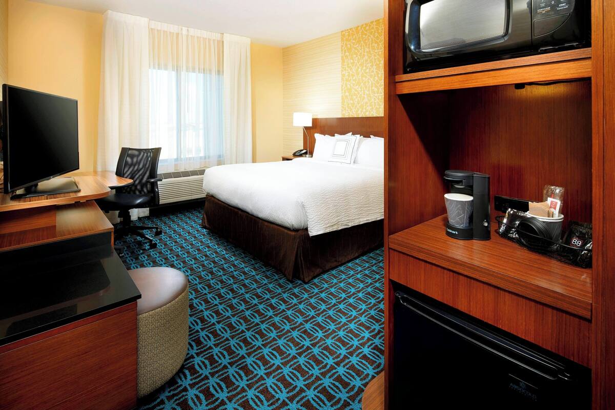 A hotel room with a bed, a desk with a computer, a coffee maker, and a microwave.
