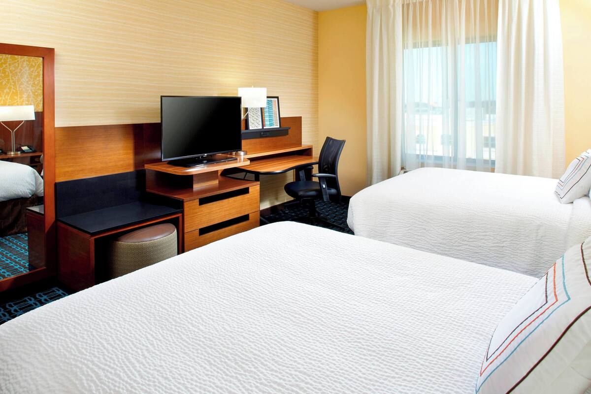 A hotel room with two beds, a desk with a television, a chair, and a small table.