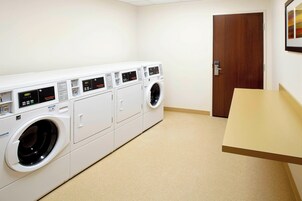 A laundry room with four front-loading washing machines, a wooden door, and a beige countertop.