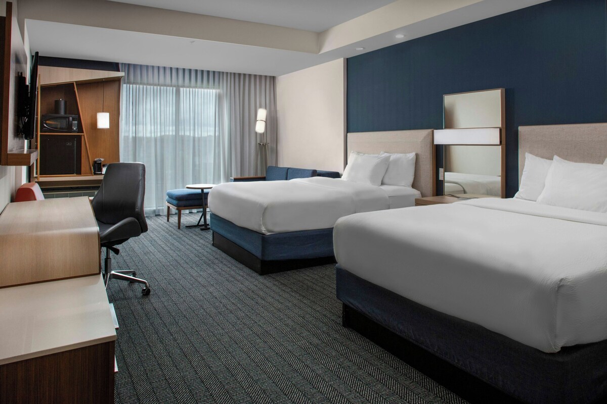 A hotel room with two beds, a desk, a chair, a small table, and a wardrobe.