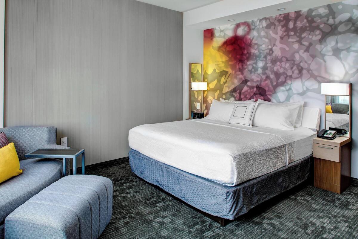 A hotel room with a bed, a sofa, a small table, and a nightstand with a lamp.