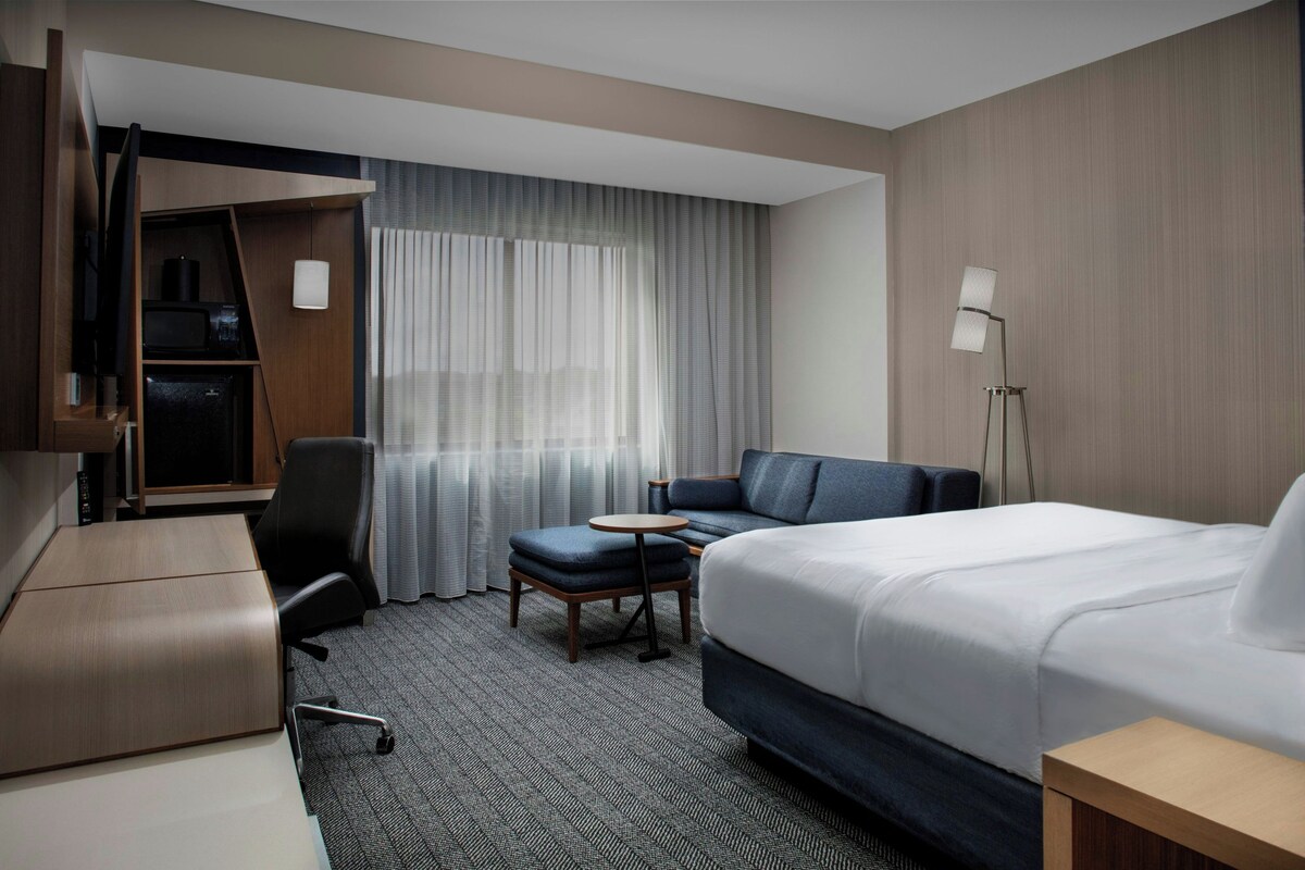 A hotel room with a bed, a desk, a chair, a small table, and a sofa.