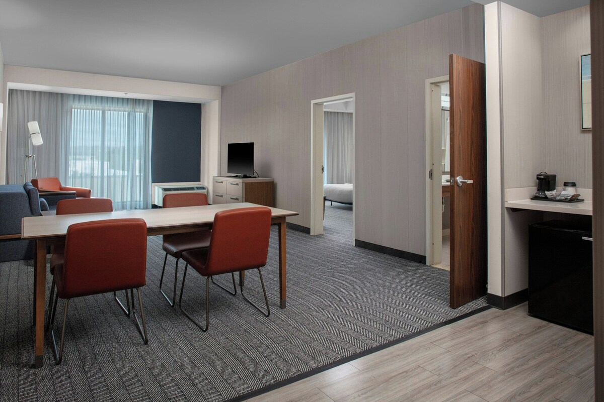 A hotel room with a dining area, a television, a bed, and a kitchenette.