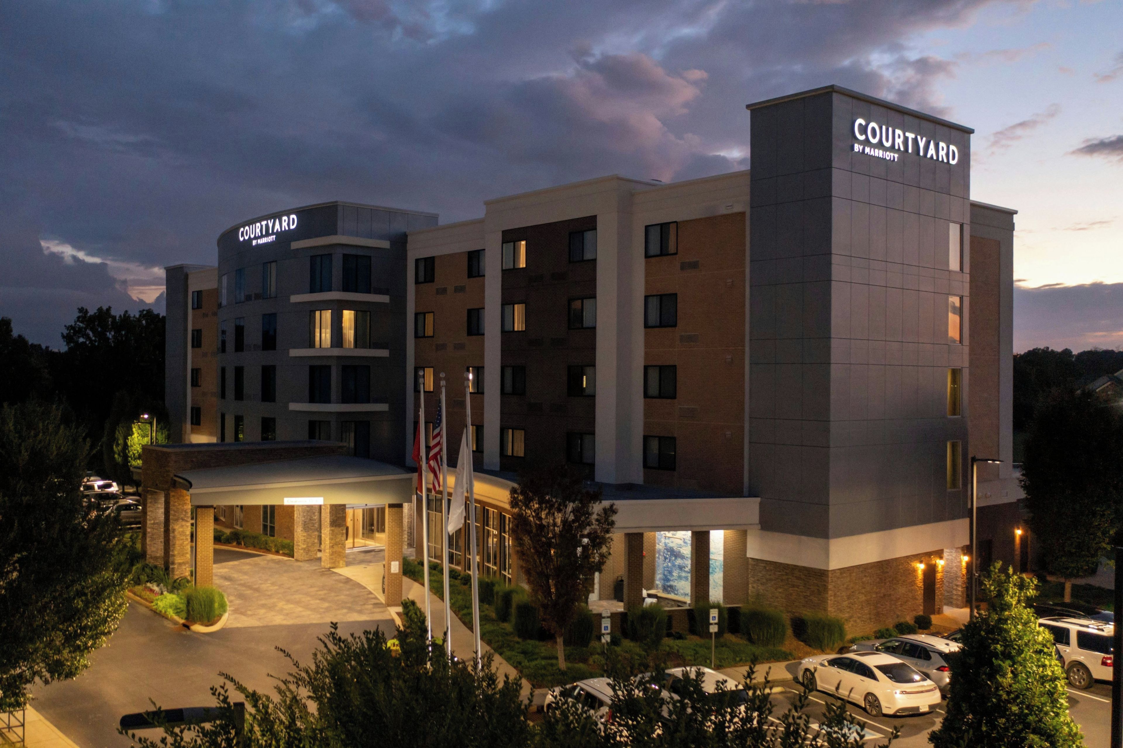 A multi-story hotel with a flat roof, a covered entrance, and a parking area with cars.