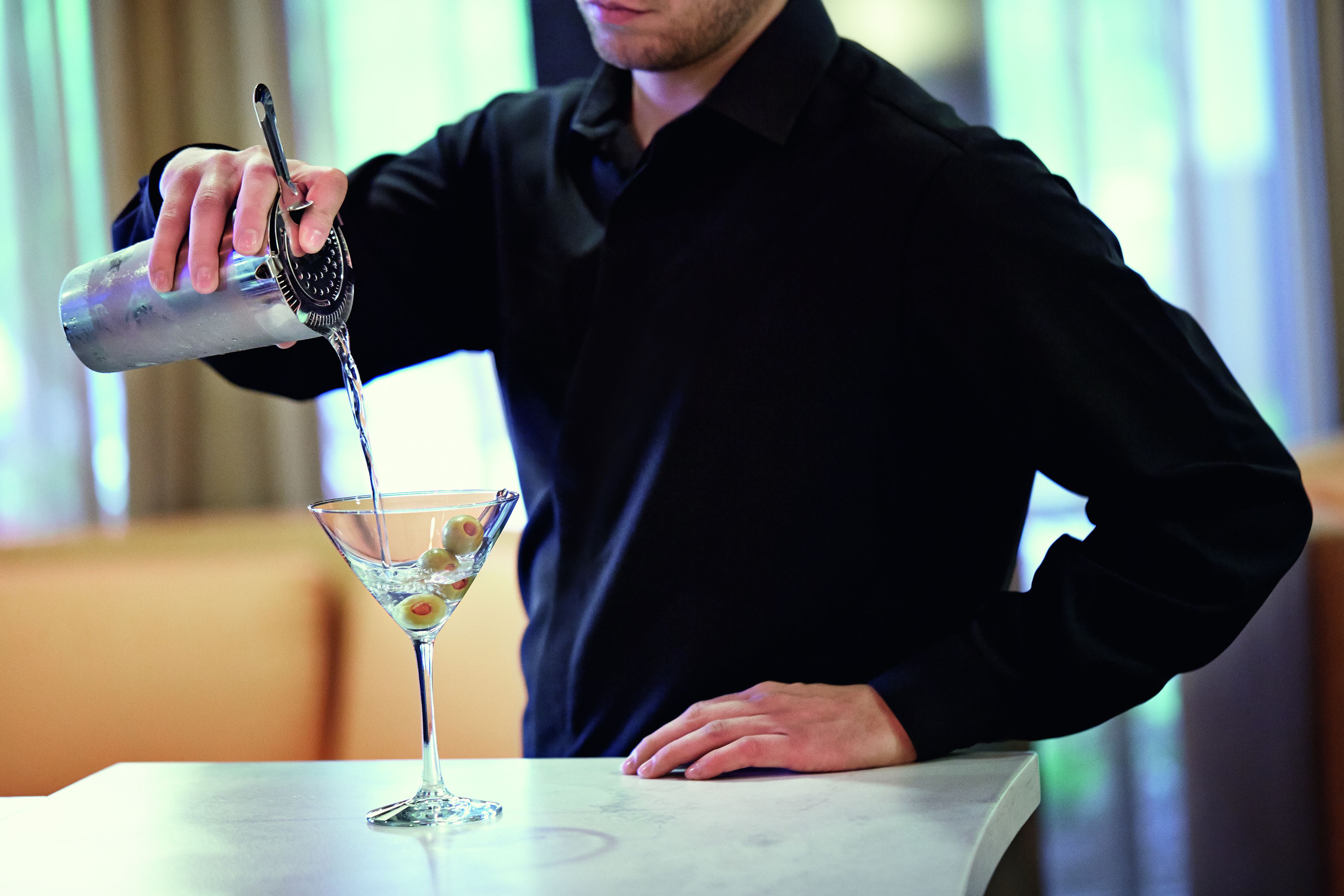 Una persona sirve una bebida en una copa de martini sobre una mesa.