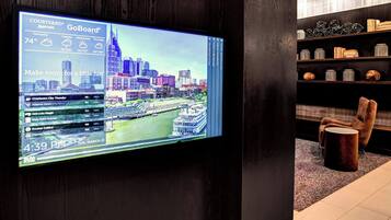 A large digital display in a hotel lobby with a cityscape view, a wooden chair, and shelves with decorative items.
