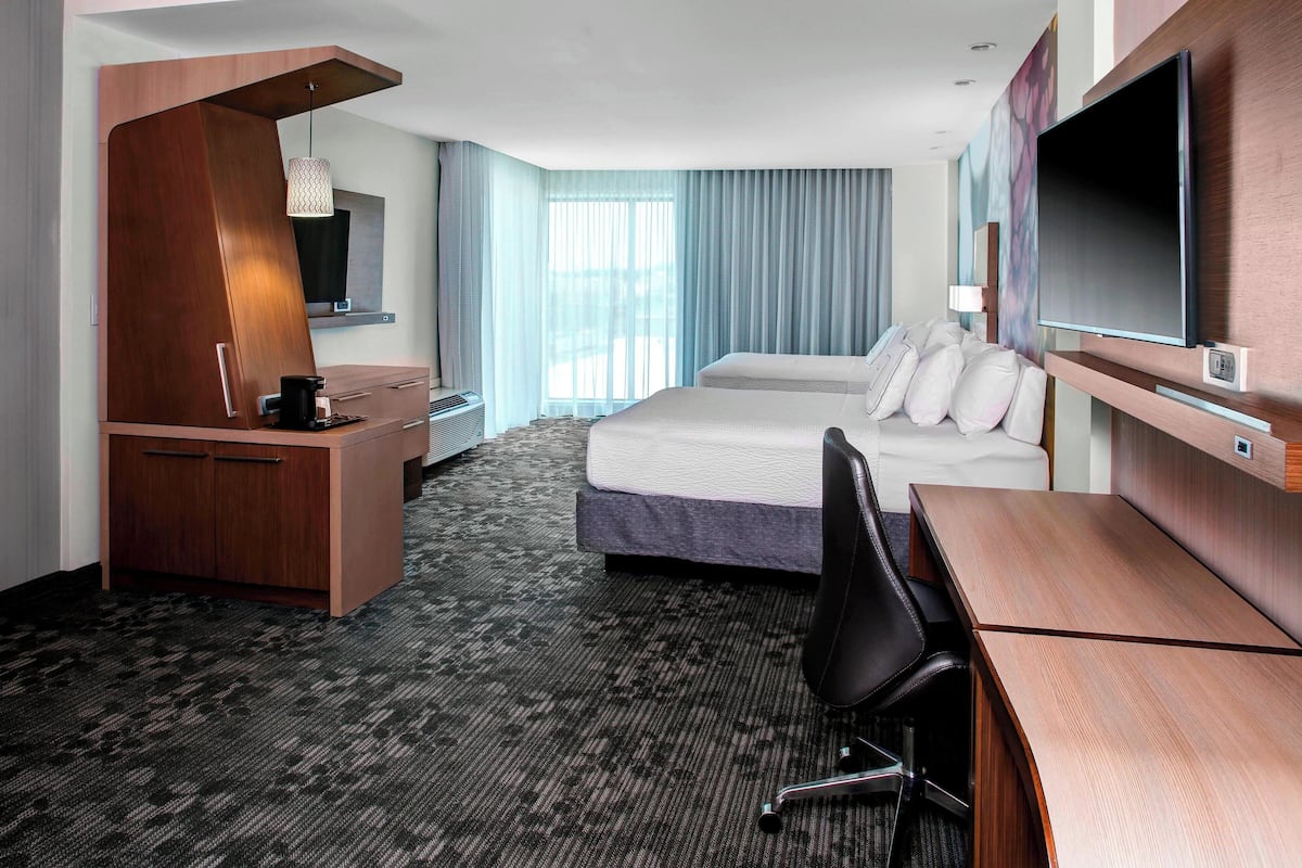 A hotel room with a bed, desk, chair, TV, and a minibar.