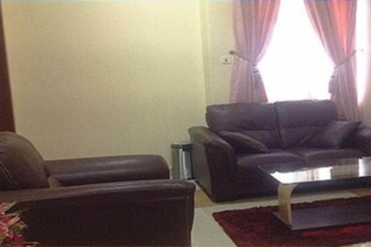 A living room with a dark leather sofa, a glass coffee table, and a red rug.