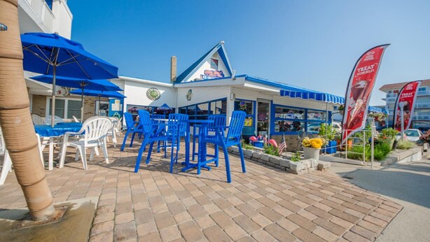 An outdoor seating area with blue chairs and umbrellas, a building with a blue and white facade, and a sign that reads "Treat Yourself." - Tangiers Motel (Wildwood Crest)