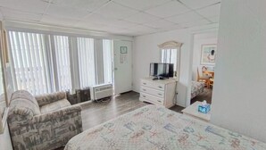 A hotel room with a bed, a sofa, a TV, a dresser, and a window with blinds. - Tangiers Motel (Wildwood Crest)