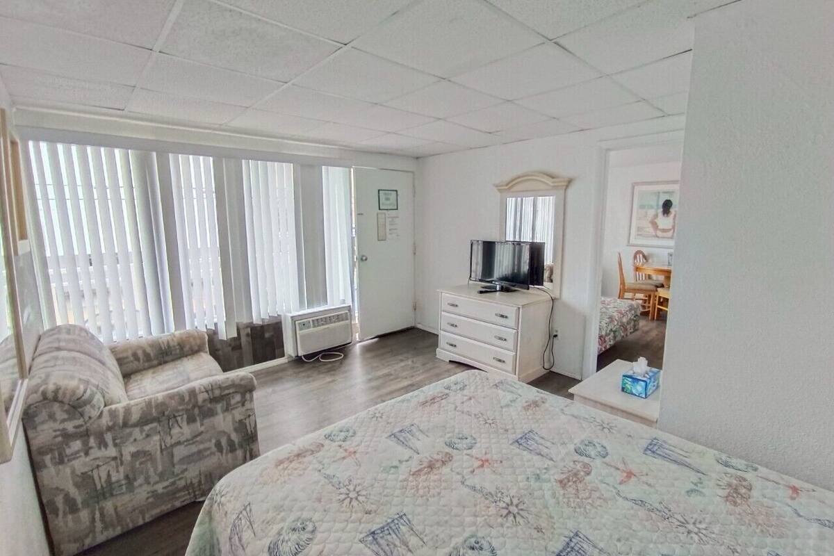 A hotel room with a bed, a sofa, a TV, a dresser, and a window with blinds.