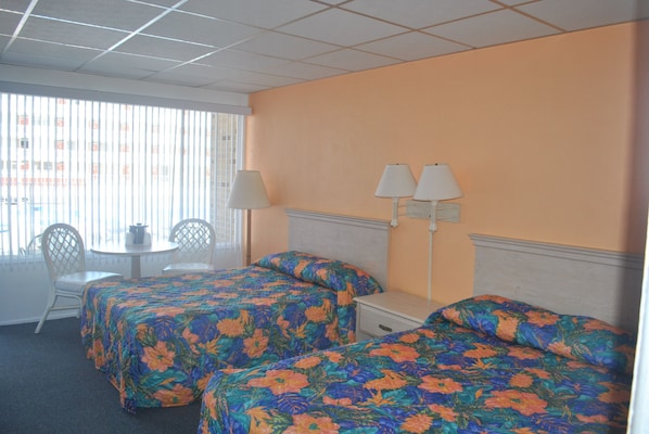 A hotel room with two beds, a small table, two chairs, and a window with blinds. - Tangiers Motel (Wildwood Crest)